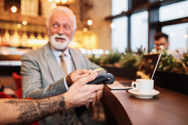 Uomo d'affari maturo che paga con carta di credito contactless con tecnologia nfc.