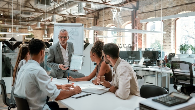 mature businessman showing something on digital tablet to young colleagues while sitting