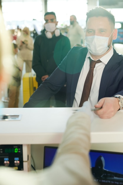 Mature businessman standing at reception counter and taking\
back his passport after registration before flight at the check\
desk