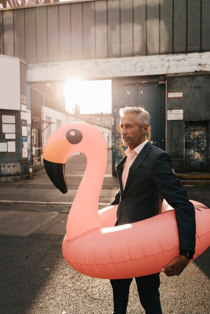 Mature businessman on the street with inflatable flamingo