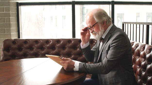 Mature businessman in a suit and glasses works on a tablet in the office. Self-development