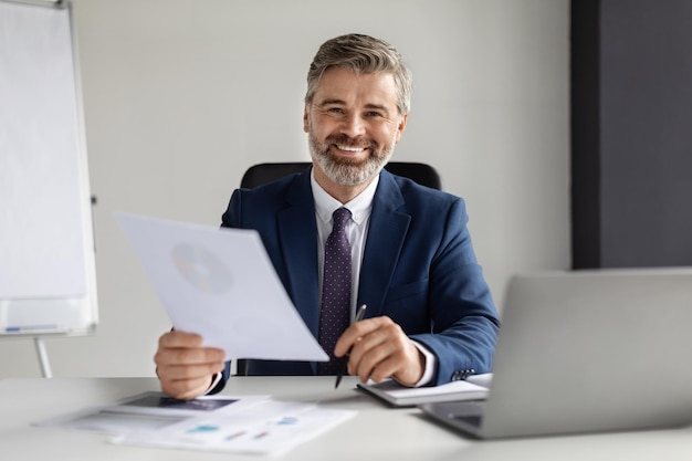 Mature businessman in suit working with documents at desk in office