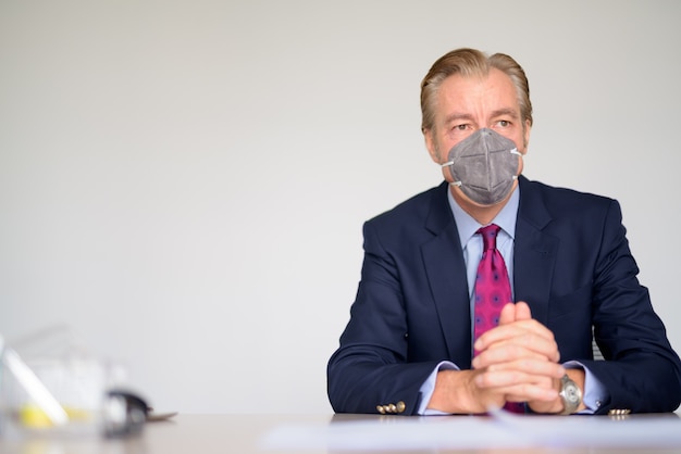 Mature businessman thinking with mask for protection from corona virus outbreak at work