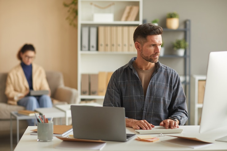 Photo mature businessman typing on computer keyboard while working at his workplace with businesswoman working in the wall