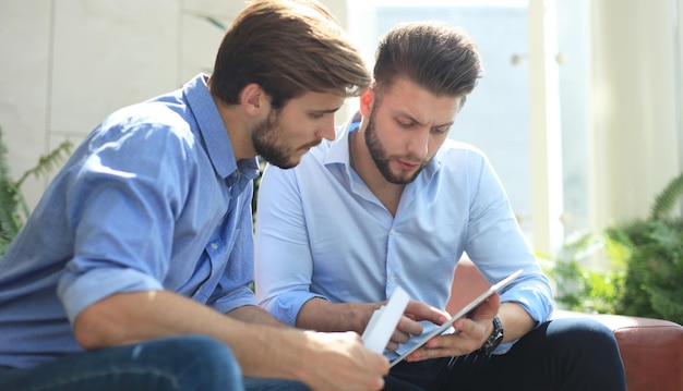 mature businessman using a digital tablet to discuss information with a younger colleague in a modern business office