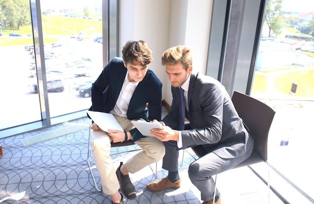 現代のビジネスオフィスで若い同僚と情報を話し合うためにデジタルタブレットを使用している成熟したビジネスマン。
