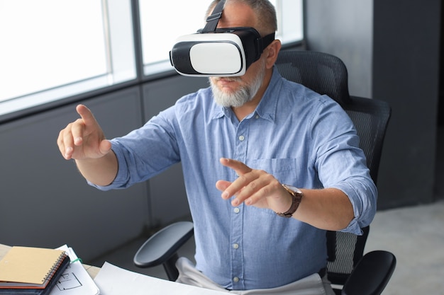 Mature businessman wearing a VR headset while sitting in modern office. Change the way you see and experience the world.