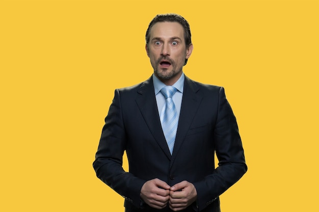 Mature businessman with facial expression of surprise. Shocked and surpised middle-aged man wearing formal suit isolated on yellow background.