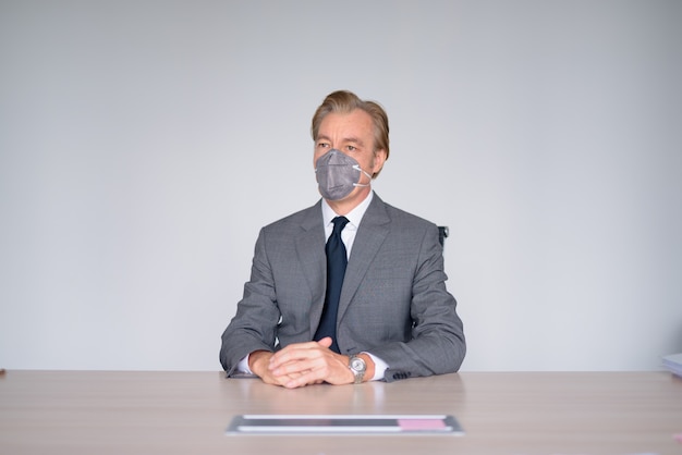 Зрелый бизнесмен, работающий с маской для защиты от вспышки коронирусного вируса на работе