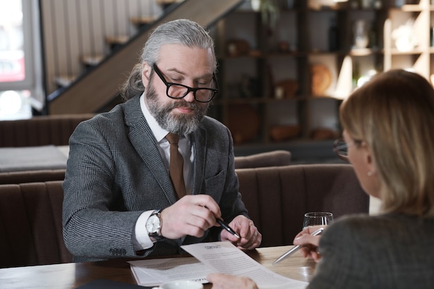 Mature businessmanin eyeglasses concluding business contract with his partner at the table in restaurant