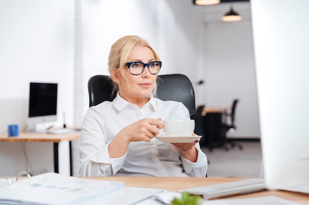 Mature businesswoman drinking coffee with pc computer at office