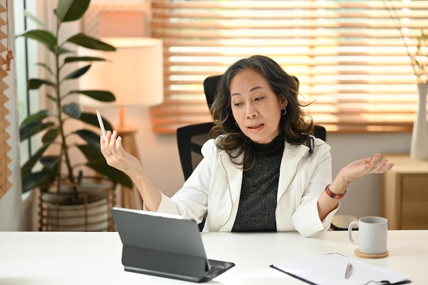 Mature businesswoman working from home having online video call on digital tablet in modern apartment