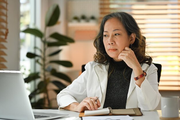 Mature businesswoman working online from home with laptop computer in winter atmosphere