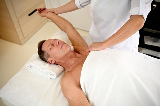 Mature caucasian man receiving professional therapeutic\
rehabilitative massage at wellness clinic. body care,\
physiotherapy, sport injury rehabilitation concept, holistic care\
concept