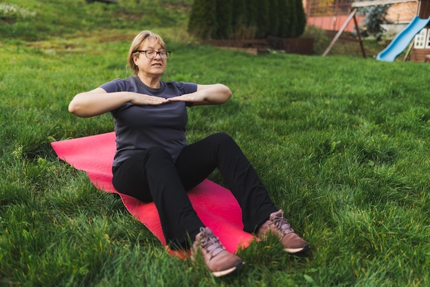 Mature caucasian retired woman in the park meditates and\
performs breathing exercises summer day