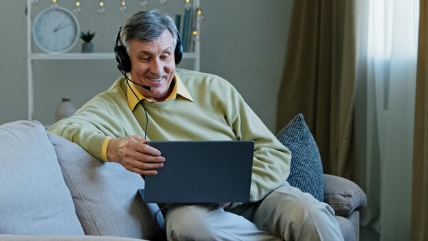 Photo mature caucasian s talking man working distantly from home sitting on couch in headset talking to