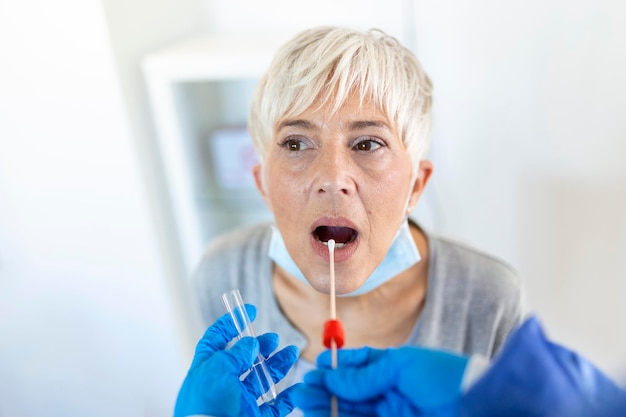 Foto donna caucasica matura in un ambiente clinico che viene tamponata da un operatore sanitario in abiti protettivi per determinare se ha contratto il coronavirus o covid19