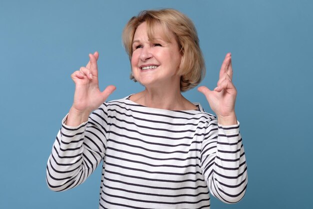 Mature caucasian woman holding fingers crossed wishing a luck