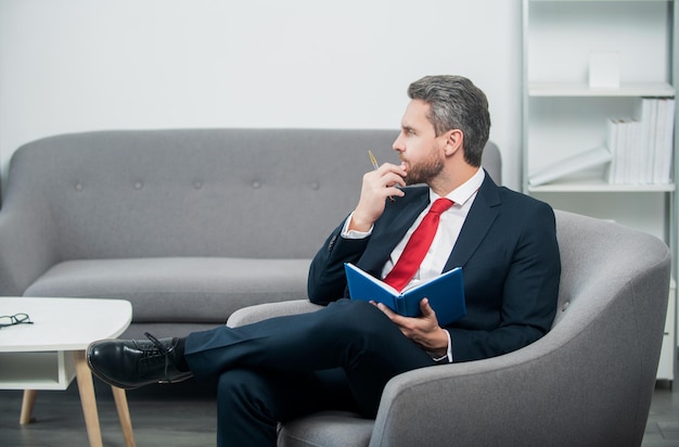 Mature ceo in suit sit in office making notes in notebook