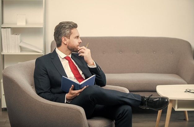 Mature ceo in suit sit in office making notes in notebook