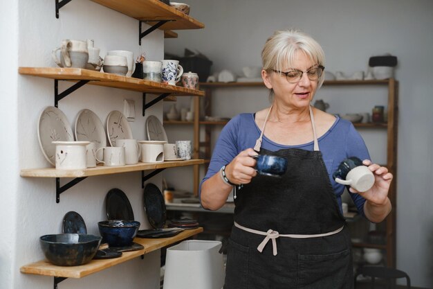 Mature ceramist standing at workshop showing her pottery