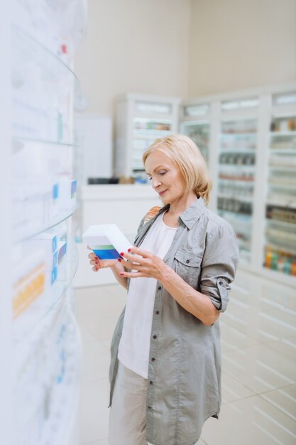 Mature client. Charming aged female keeping smile on her face while choosing medicine