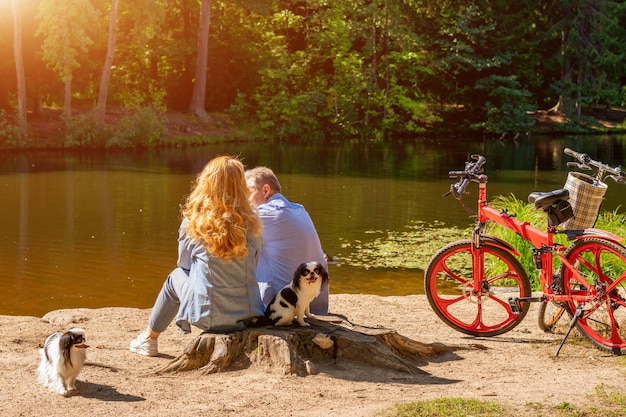 犬と太陽の下で座っている自転車と湖のほとりに成熟したカップル