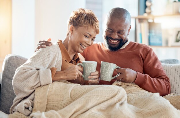 熟年夫婦はソファでコーヒーを飲み、愛のケアや簡単なライフスタイルのリビングルームで面白い冗談を笑いながら、笑顔の黒人夫婦は幸せな会話のために家でラウンジやお茶をリラックスする