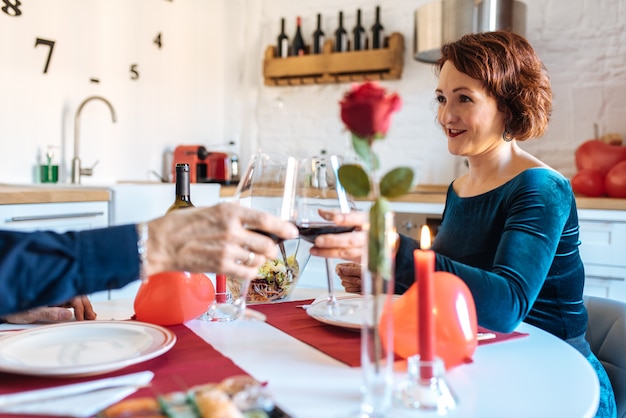 Coppie mature che hanno una cena romantica a casa per il giorno di biglietti di s. valentino e che fanno pane tostato con vino rosso