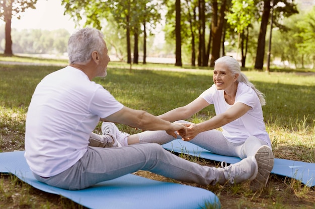 Mature couple holding hands while stretching their legs on yoga mat