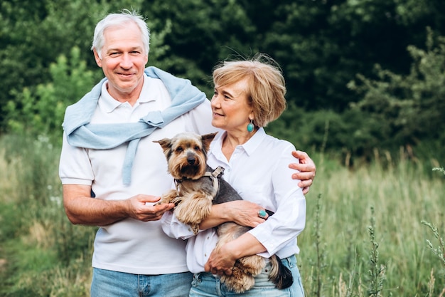 A mature couple is walking with a dog in a park