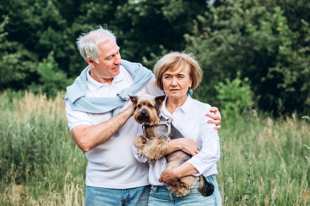 A mature couple is walking with a dog in a park