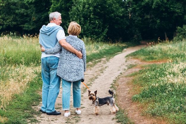 Mature couple is walking with dog in park