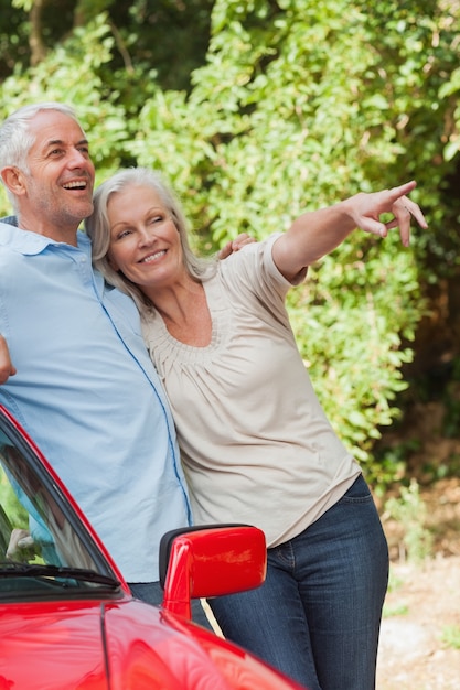 Mature couple leaning against their red cabriolet