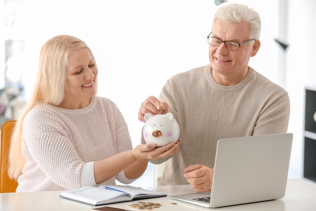 Mature couple putting coin into piggy bank at home Thinking over pension plan