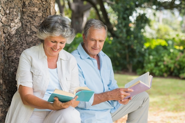 Mature couple reading books together sitting on tree trunk