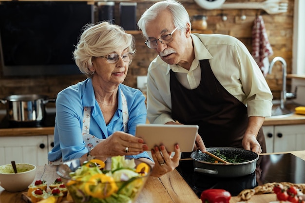 Coppia matura leggendo la ricetta sulla tavoletta digitale mentre si prepara il pranzo in cucina