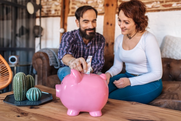 Mature couple relaxed at home in the sofa saving money on the piggy bank