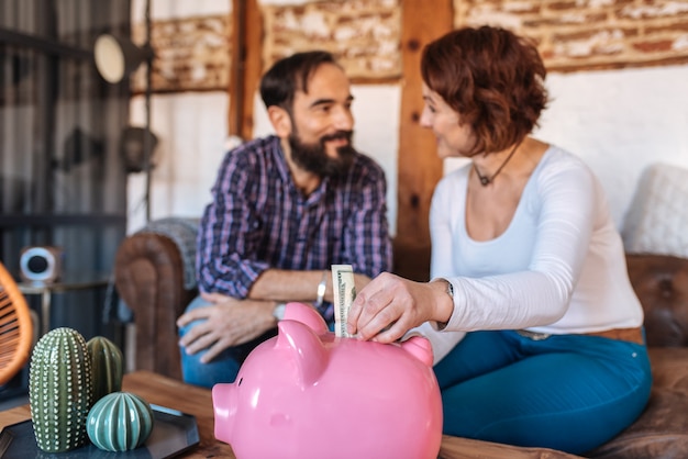 Mature couple relaxed at home in the sofa saving money on the piggy bank