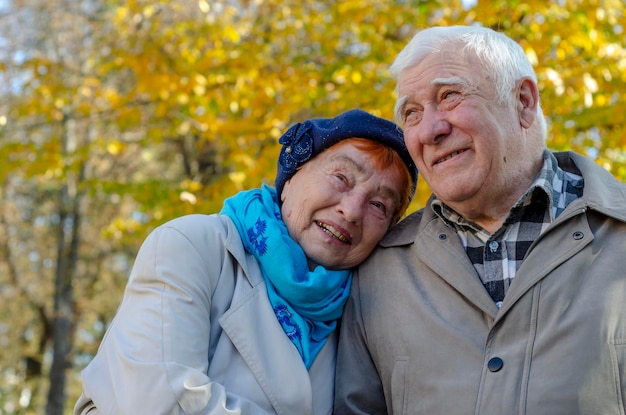 Пожилая пара, сидящая в осеннем парке, шутит, вспоминает молодость и смотрит вверх