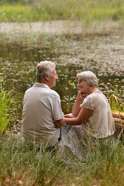 Mature couple sitting on green grass near summer pond