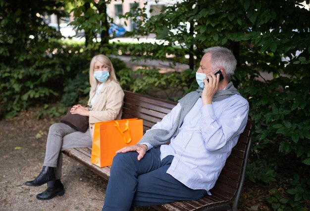 Mature couple sitting at the sides of a bench to keep distance