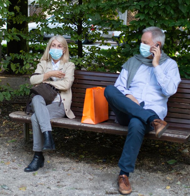 Mature couple sitting at the sides of a bench to keep distance