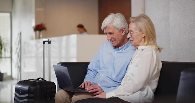 Mature couple sitting on sofa at hotel lobby and using laptop