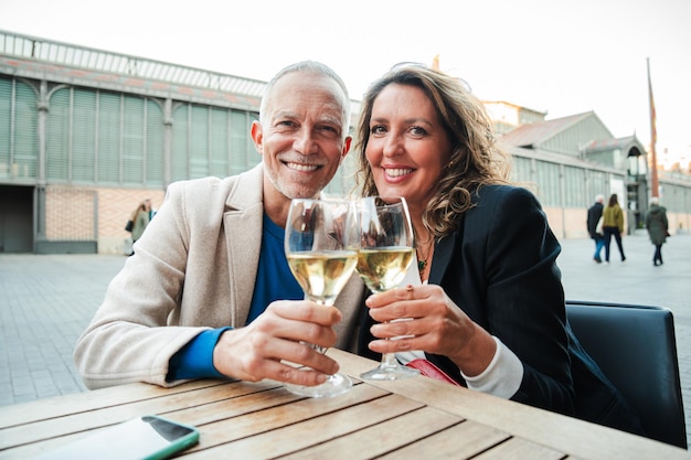 Photo mature couple toasting white wine glasses smiling and looking at camera middle aged married people