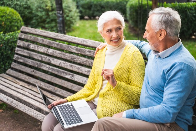 Mature couple using computer laptop on a bench