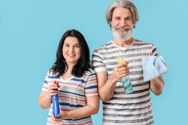 Mature couple with cleaning supplies on color surface