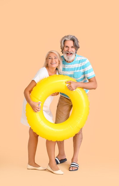 Mature couple with inflatable ring on color background