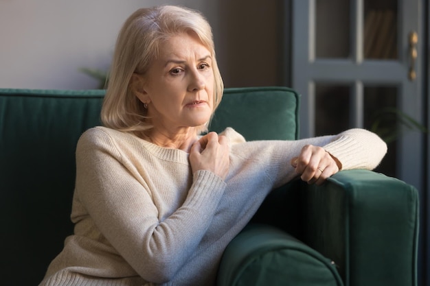 mature depressed woman lost on thoughts sitting on couch