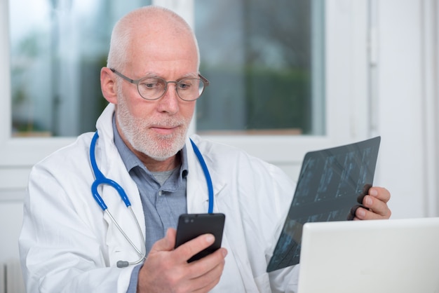 Mature doctor looking at x-ray picture and using  telephone